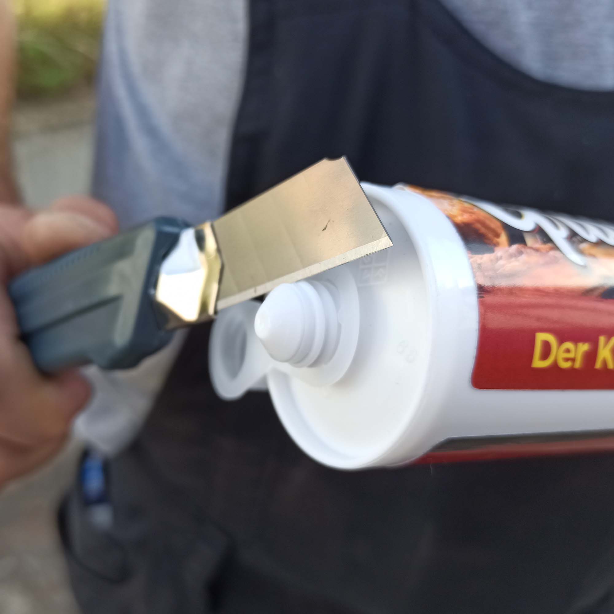 Nahaufnahme: Cuttermesser öffnet eine 300-ml-Kartusche aus dem Grillikon Geschenkset „WM-Edition“ mit Senf, Currysoße und weißer BBQ-Soße samt Zubehör und T-Shirt.